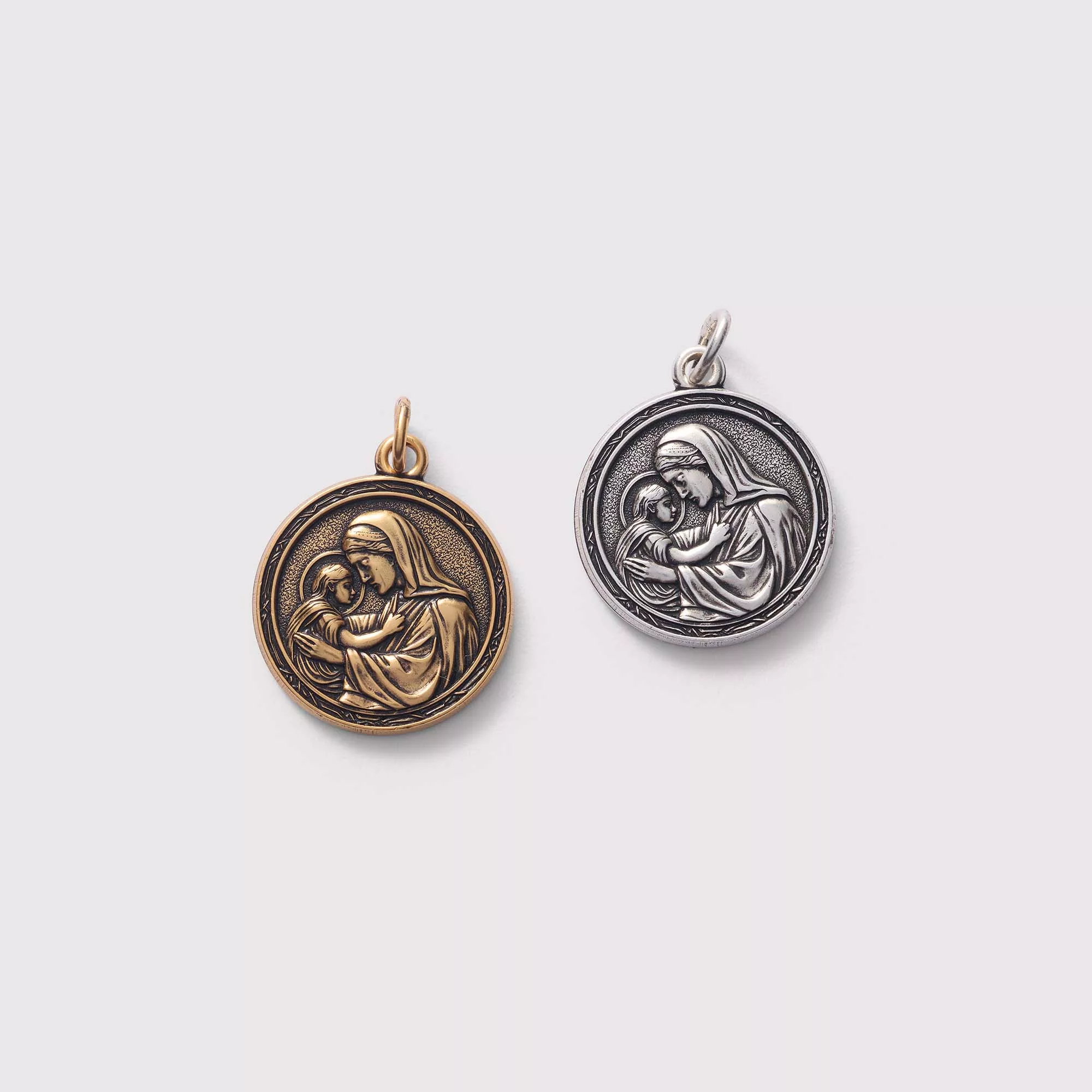 Two religious pendants featuring a mother and child design on a light gray background.