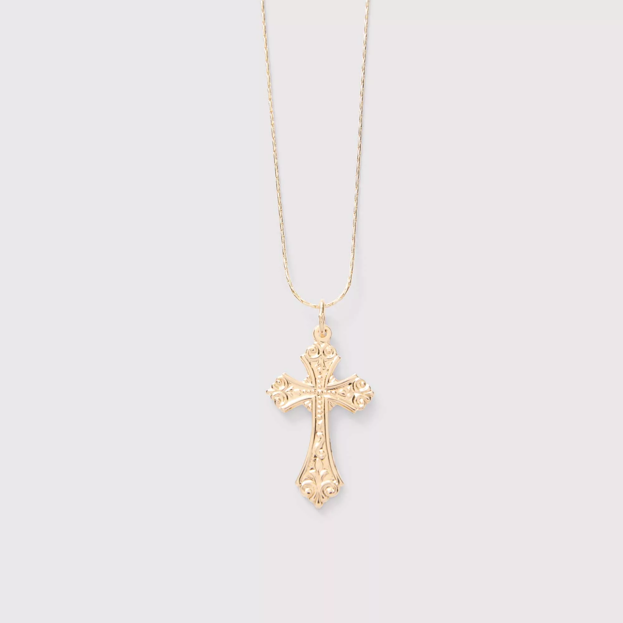 Gold cross necklace on a light gray background