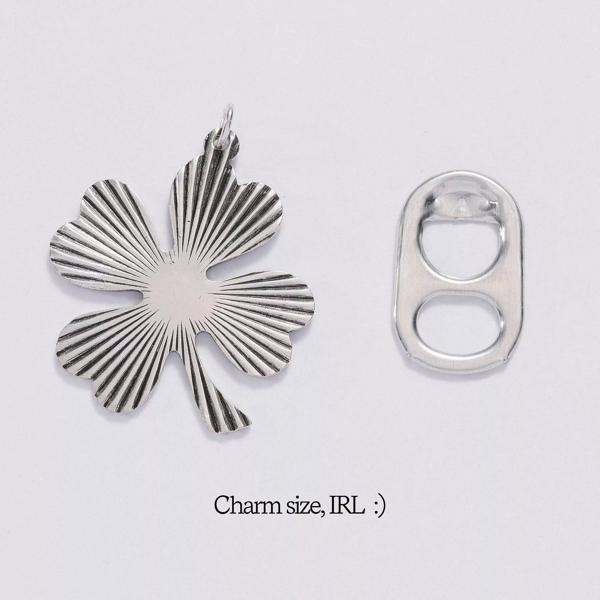 &LIVY Shine On Clover Charm in silver shown next to soda tab for size comparison with text Charm size IRL four-leaf clover with radial sunburst texture