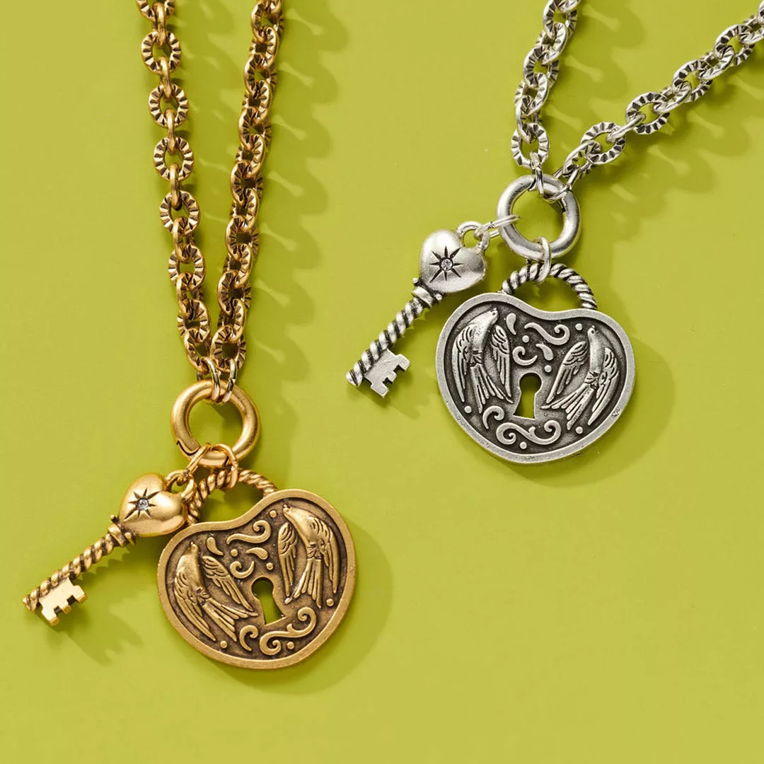 &LIVY The Key to Us Chain Necklace Set in both antique gold and antique silver close-up of ornate heart-shaped lock pendants with angel wing design and key charms with gemstone accents on green background