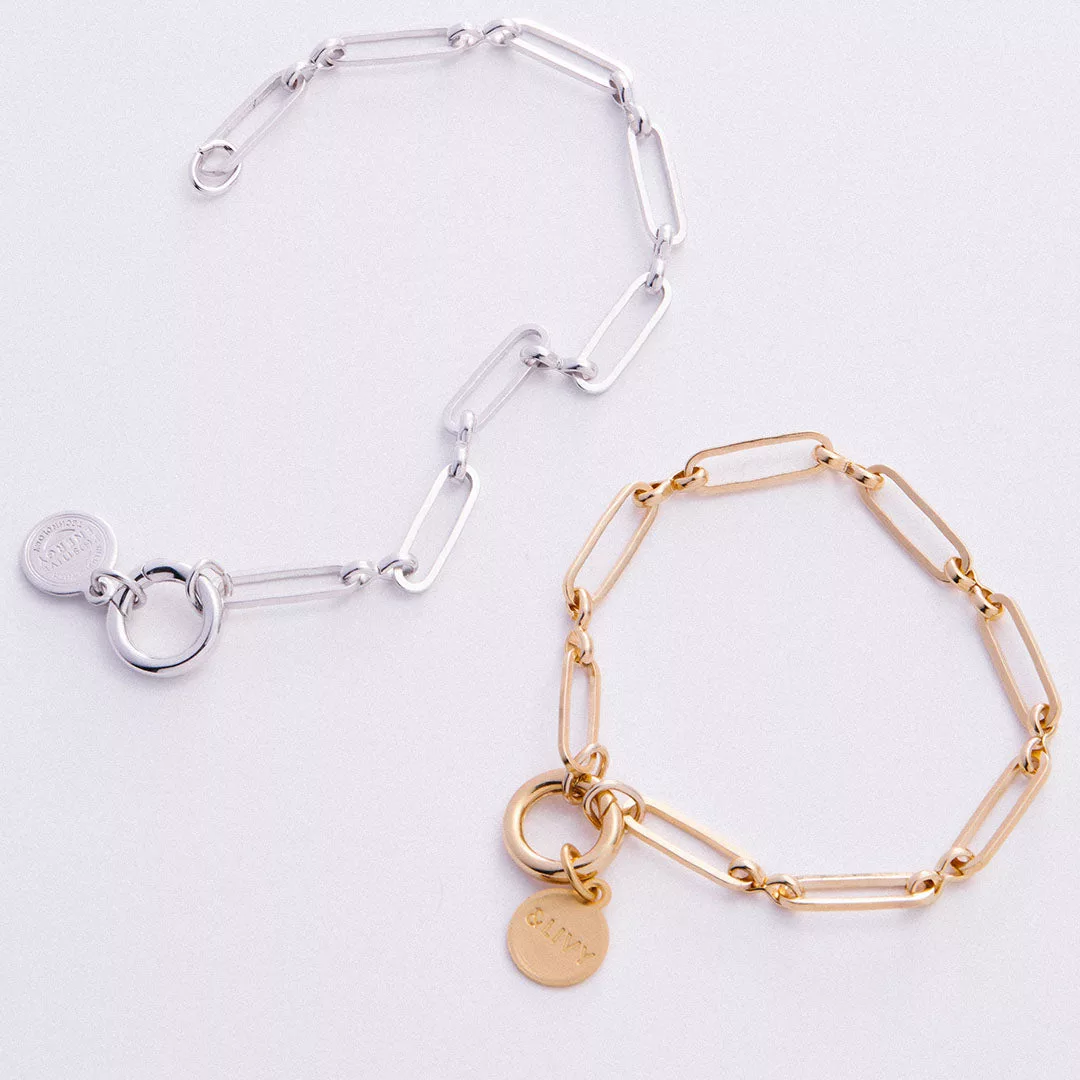 &LIVY Paperclip Intention Chain Bracelet in both finely finished silver and finely finished gold showing elongated paperclip links with round interlocking ring charm holders and branded coin charms displayed together on white background