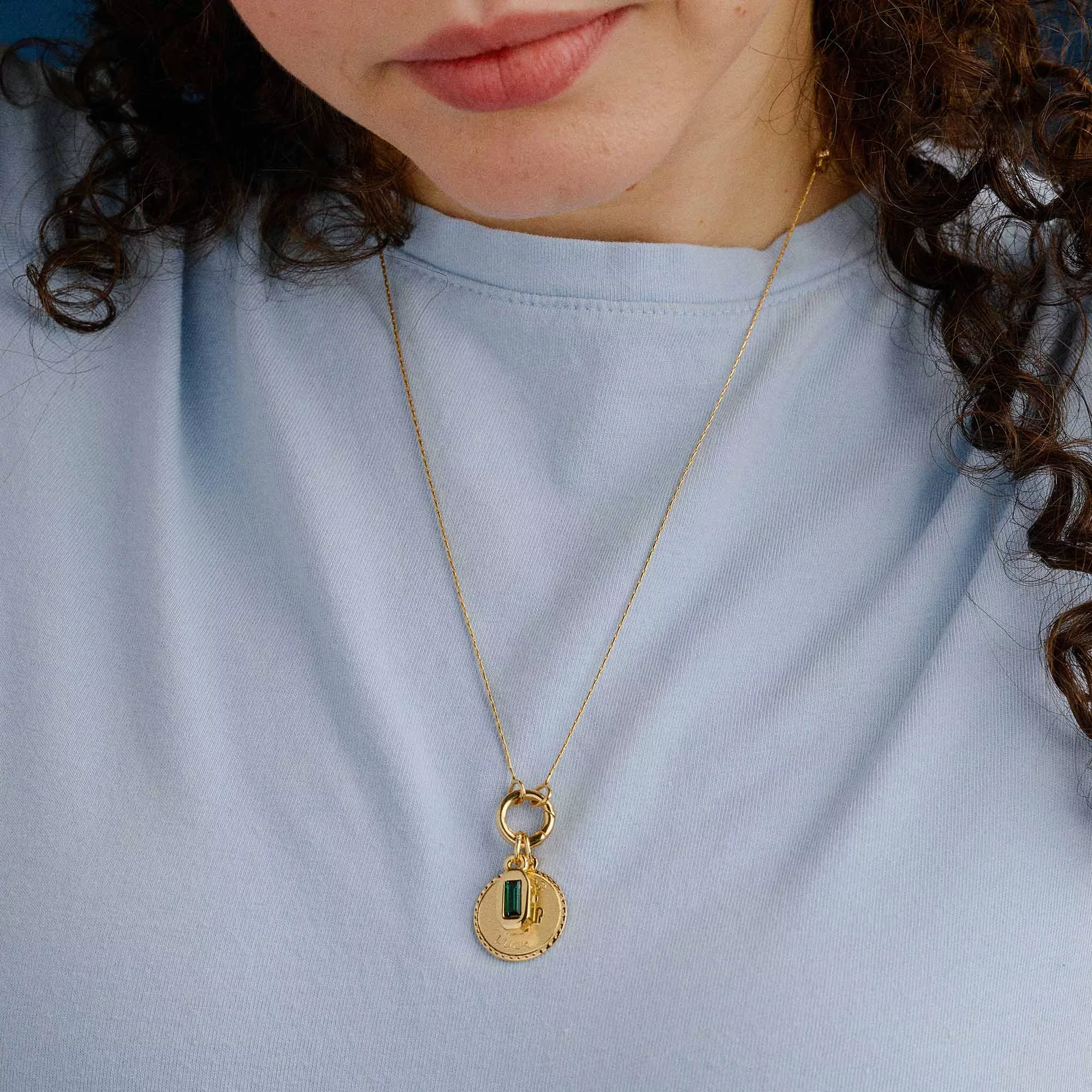&LIVY Renewed Love Expandable Necklace in gold worn by model showing Good Luck Token charm and emerald crystal pendant on expandable chain