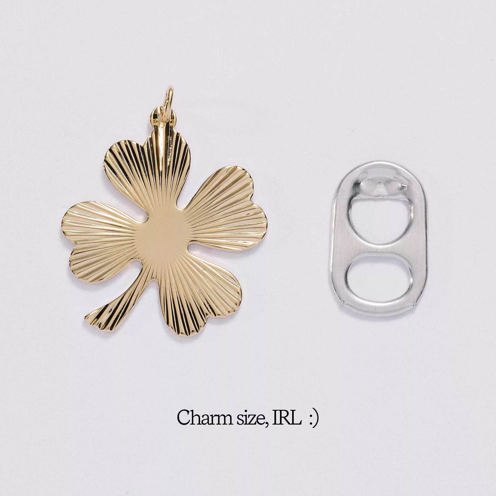 &LIVY Shine On Clover Charm in gold shown next to soda tab for size comparison with text Charm size IRL four-leaf clover with radial sunburst texture
