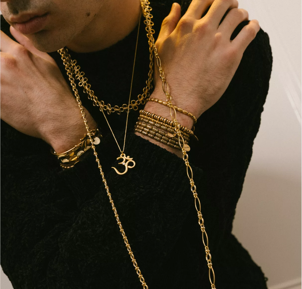 Close-up of a person wearing multiple gold necklaces and bracelets on a black sweater.