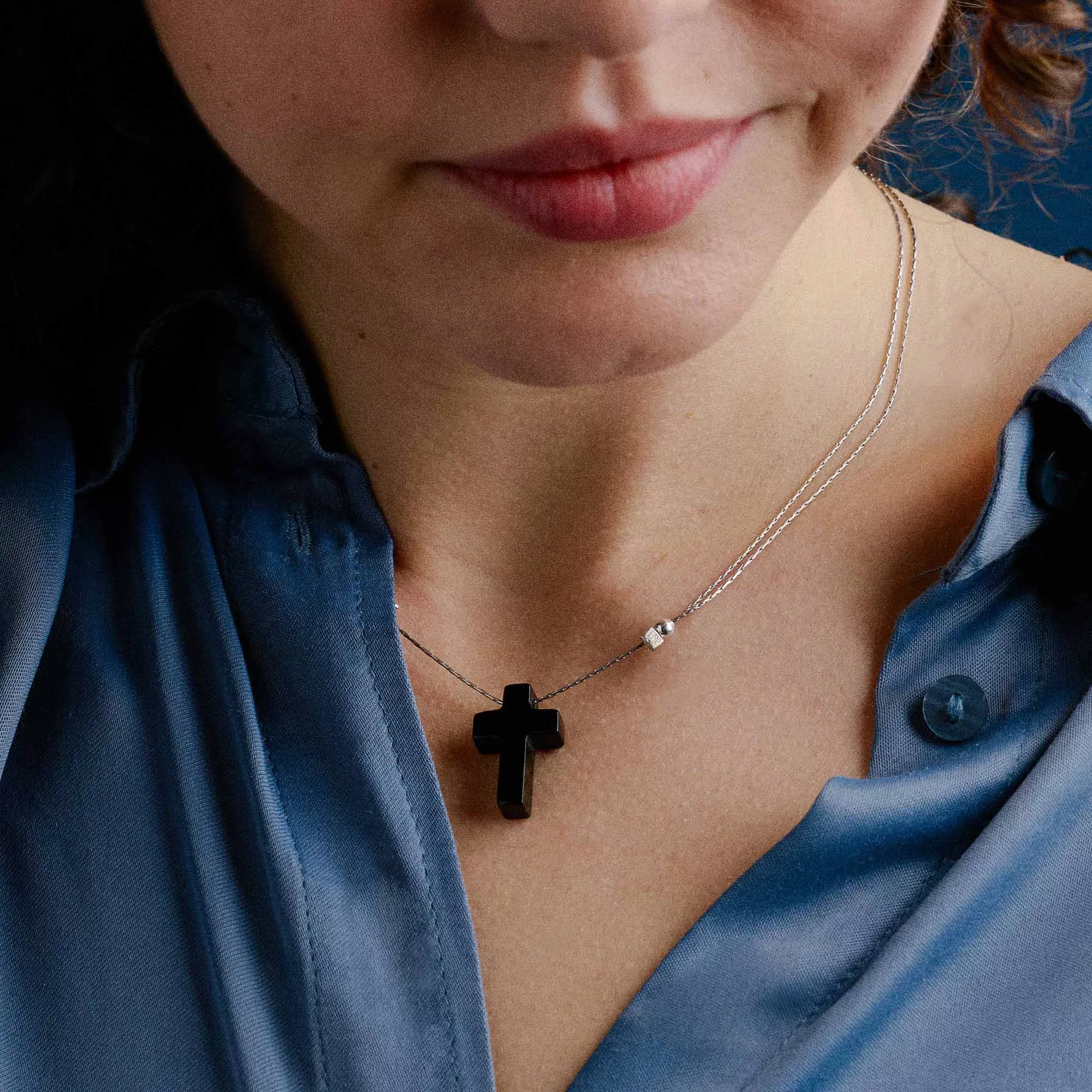 &LIVY Onyx Cross Expandable Necklace in finely finished silver worn by model showing polished black onyx cross pendant on delicate silver slider chain styled with blue satin top