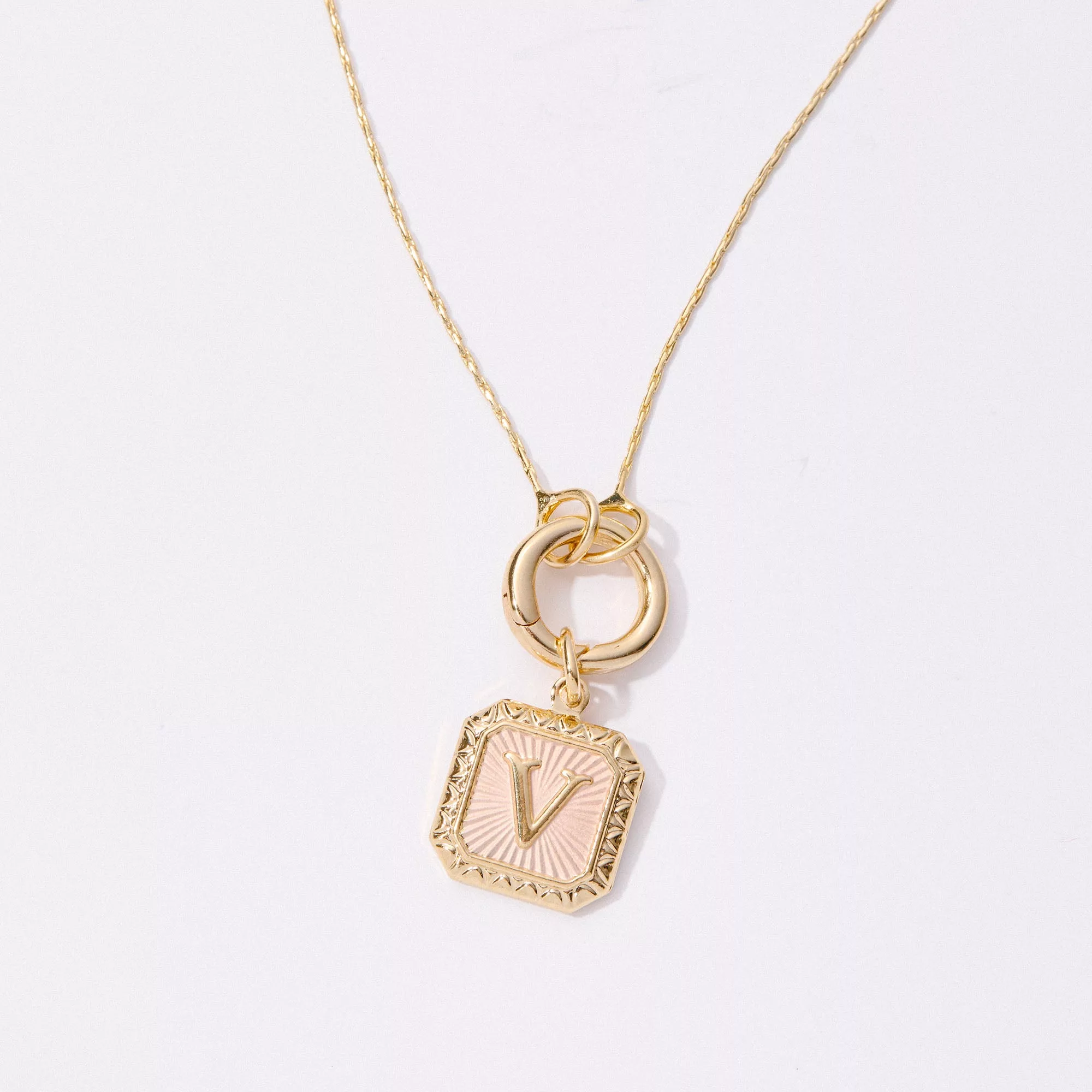&LIVY Expandable Intention Chain Charm Necklace close-up of gold interlocking ring clasp with pink enamel letter charm featuring radial sunburst texture on delicate gold chain