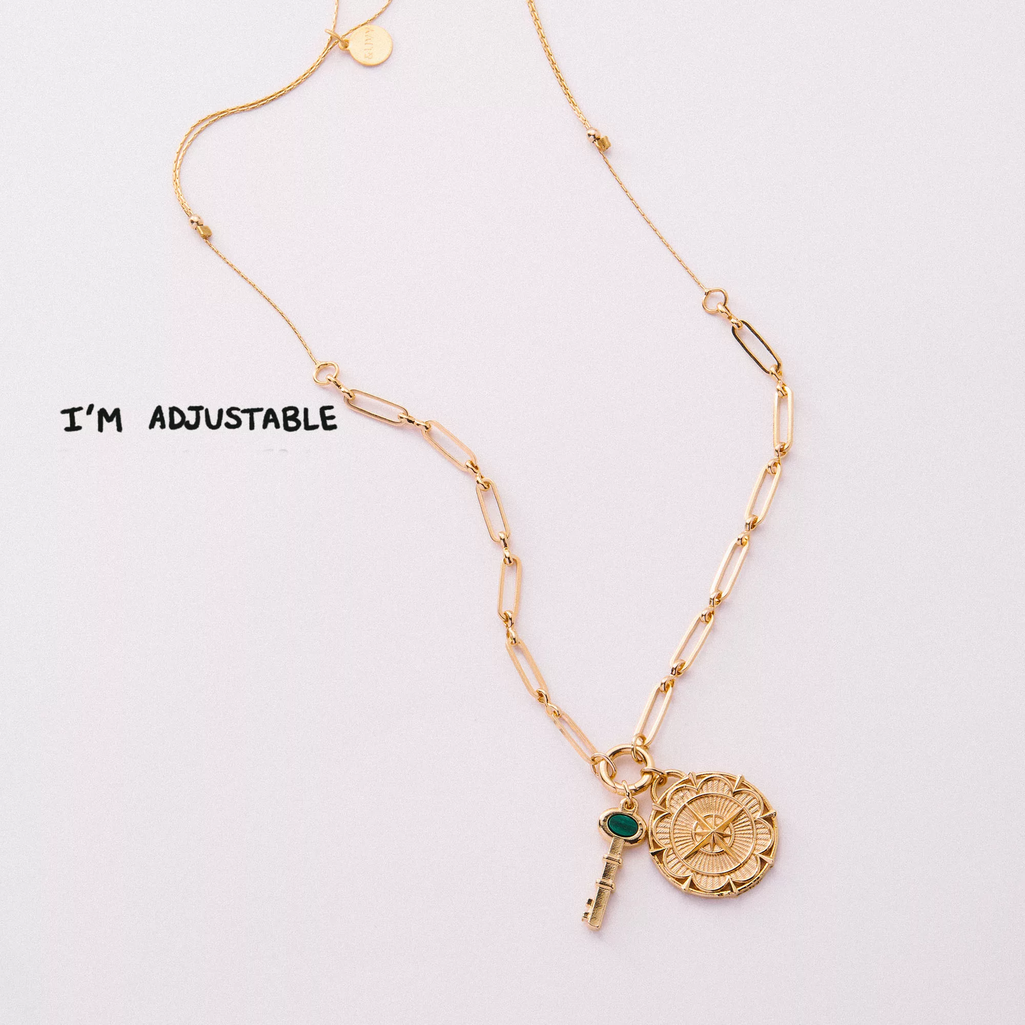 &LIVY Paperclip Intention Chain in finely finished gold full length view with text I'm Adjustable featuring signature medallion charm with compass star design and green gemstone accent on elongated paperclip link chain