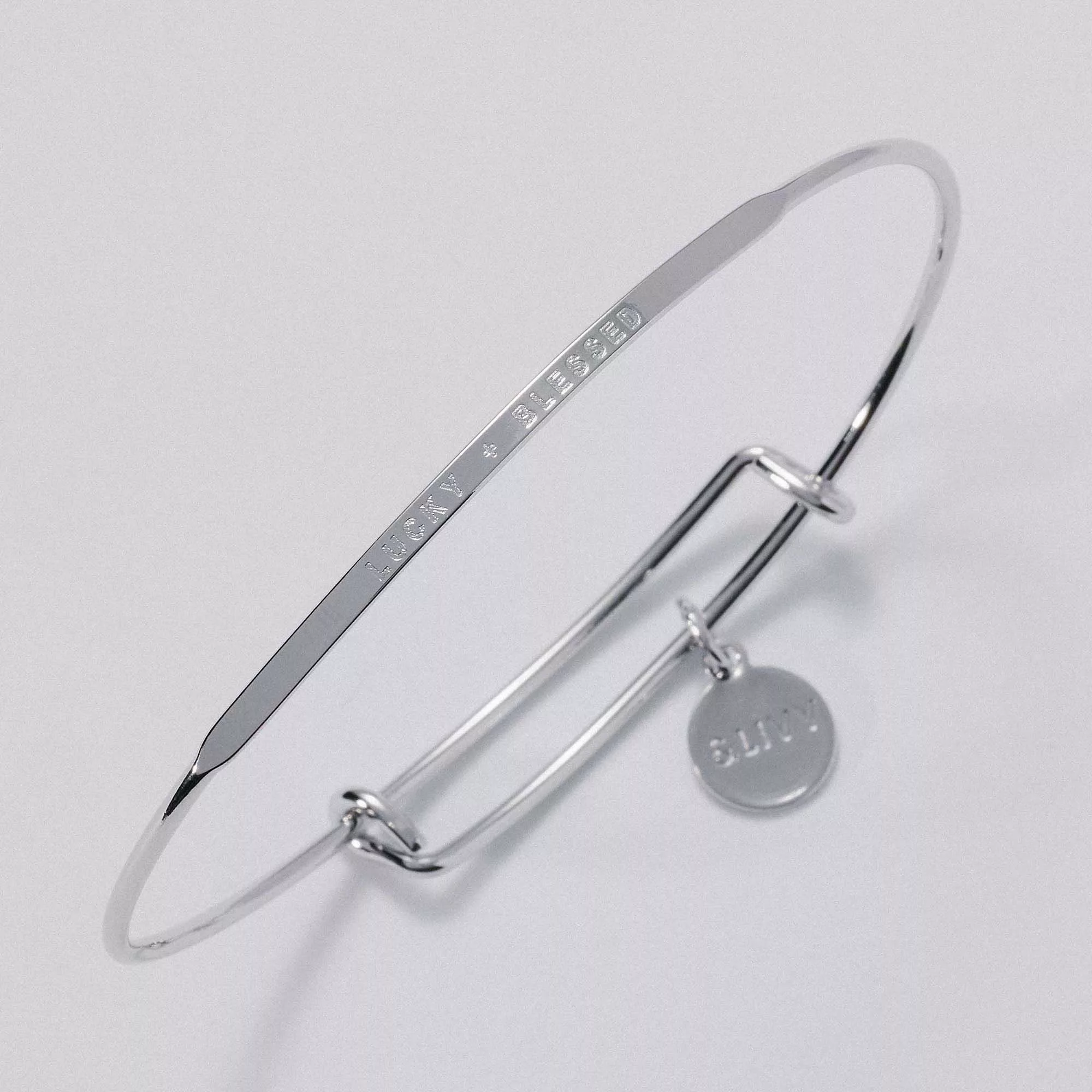 &LIVY Lucky + Blessed Posy expandable bangle in silver with 'LUCKY + BLESSED' engraving and &LIVY charm